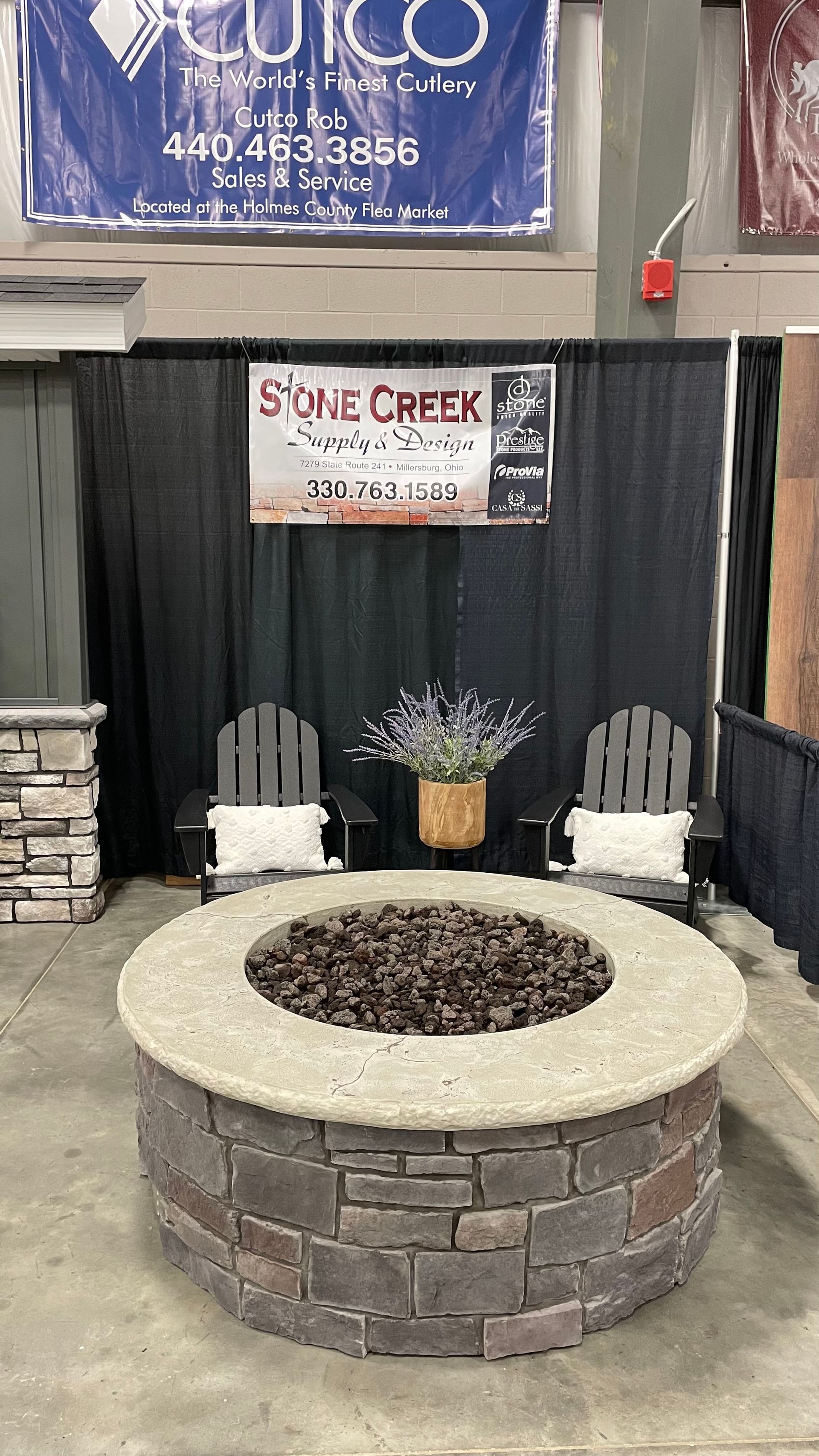 Fire pit display with chairs and flowers in front of a backdrop, showcasing Stone Creek Design.
