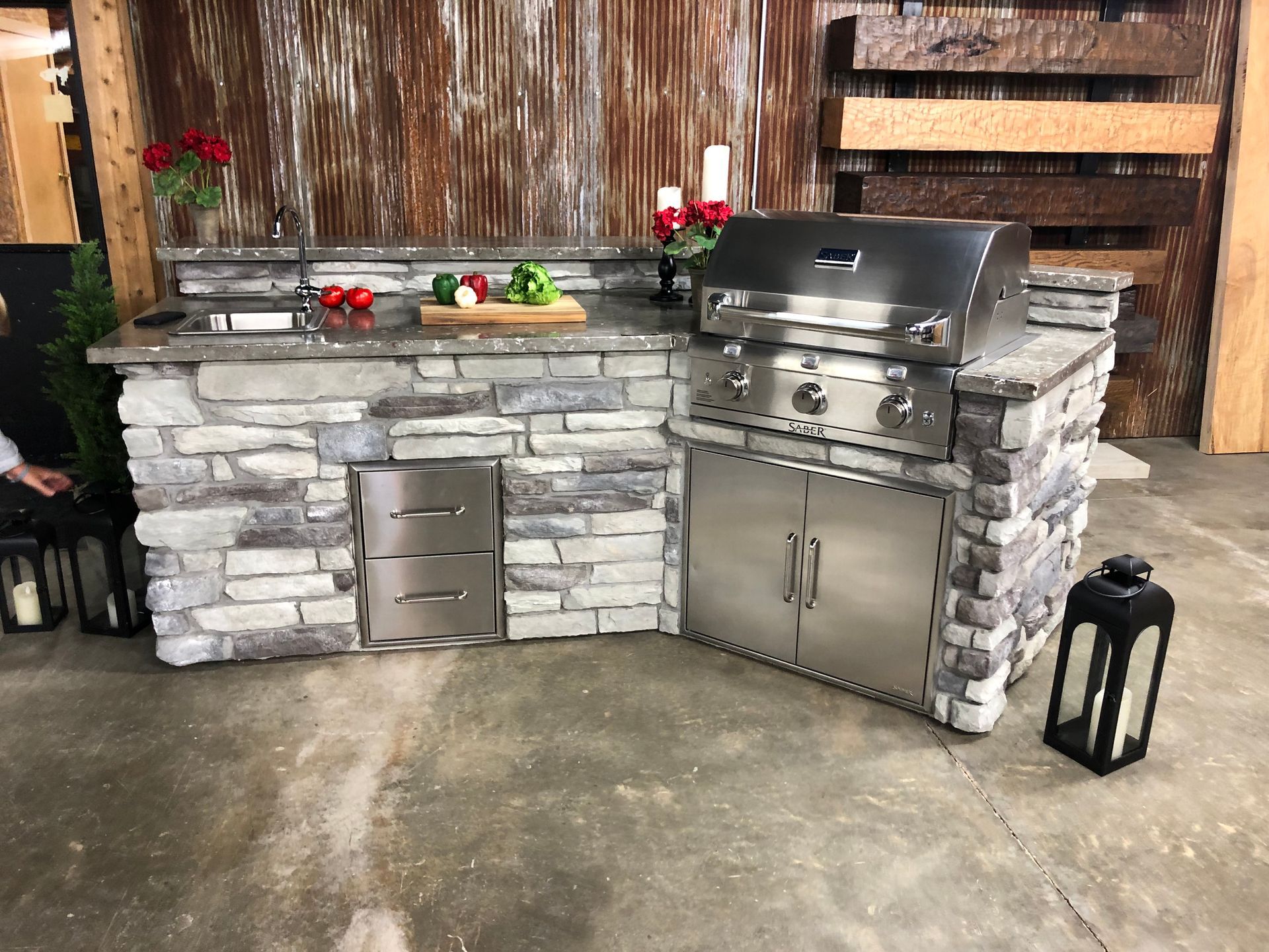 Outdoor kitchen with stone facade, stainless steel grill and appliances, wooden accents.