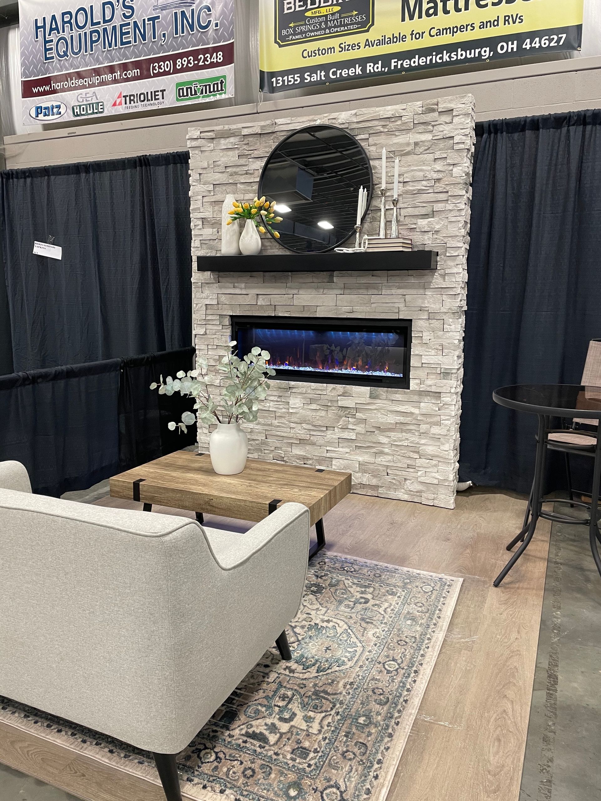 Cozy living room display with a stone fireplace, sofa, rug, and decorative items.