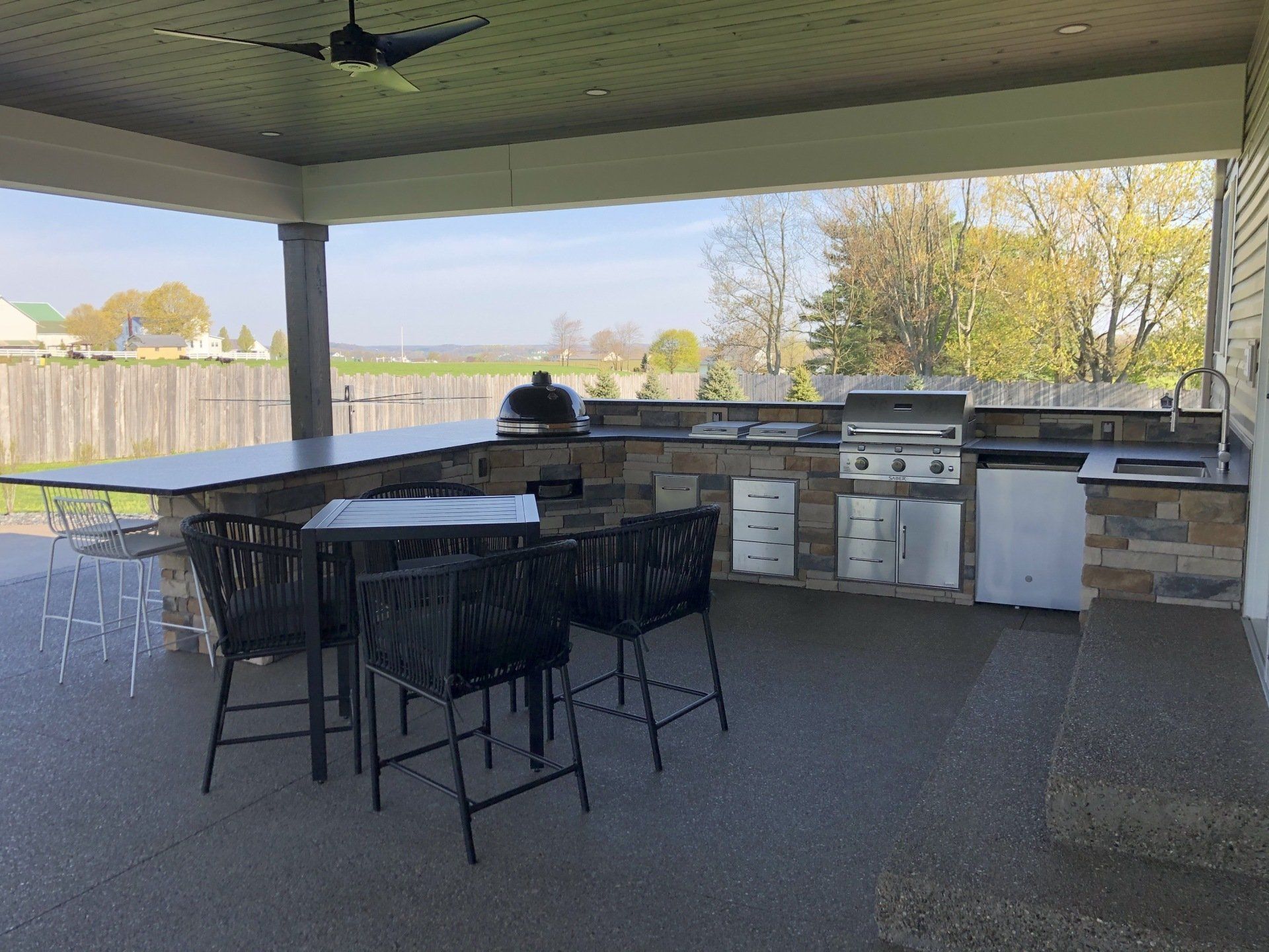 Covered outdoor kitchen with grill, seating, and scenic view.