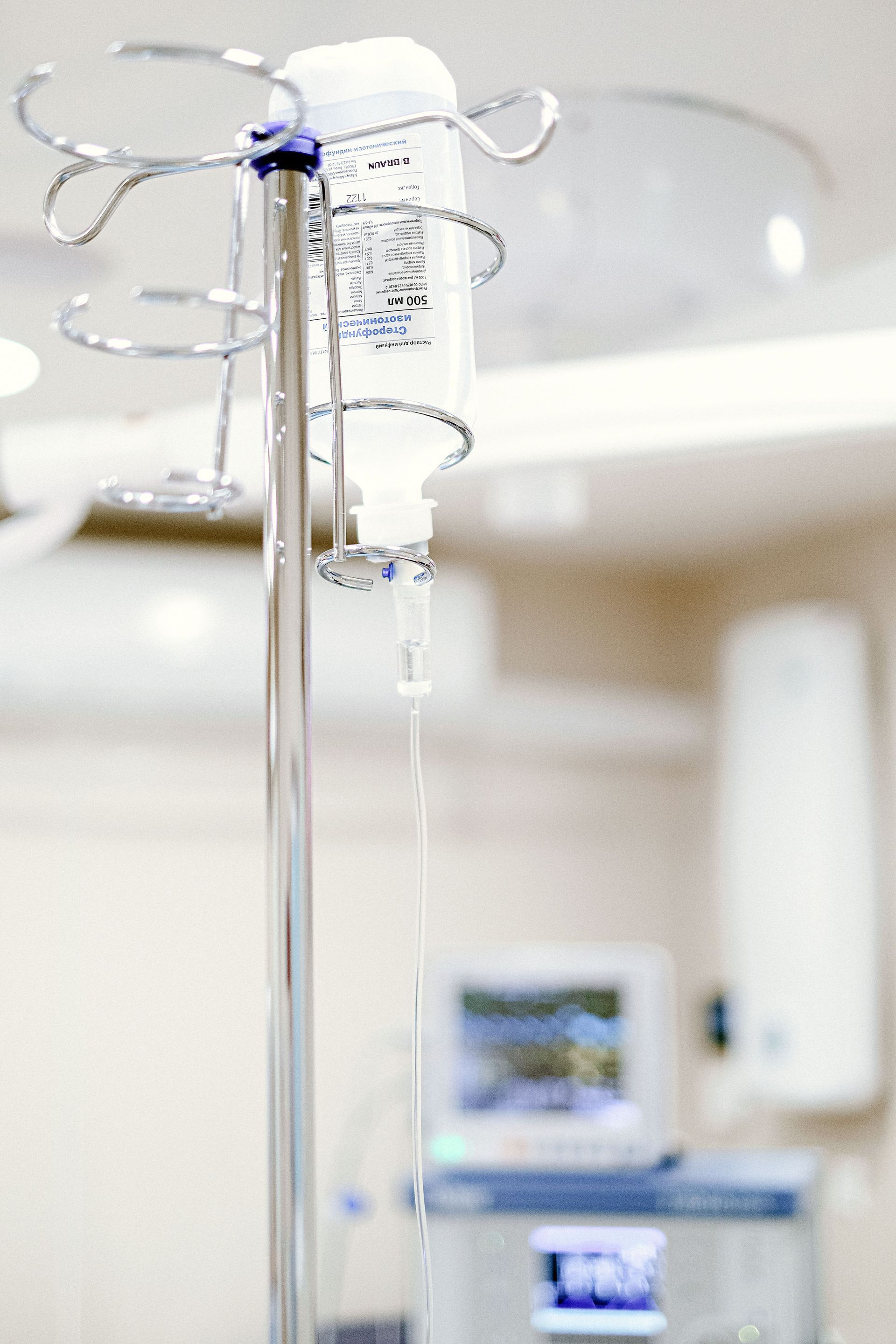 IV drip on a metal stand in a hospital room with medical equipment in the background