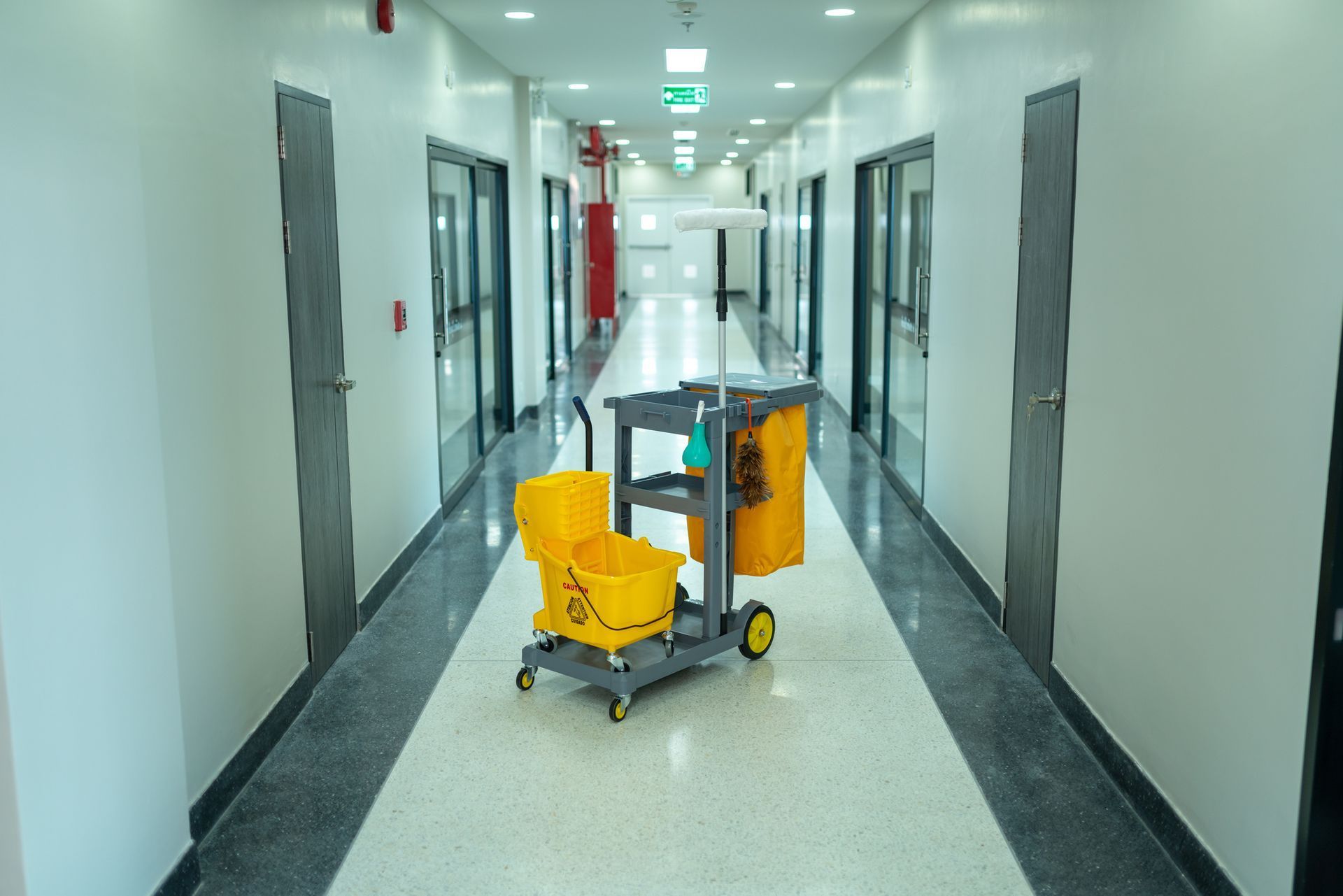 Empty hospital corridor with a yellow cleaning cart and mop bucket in the center