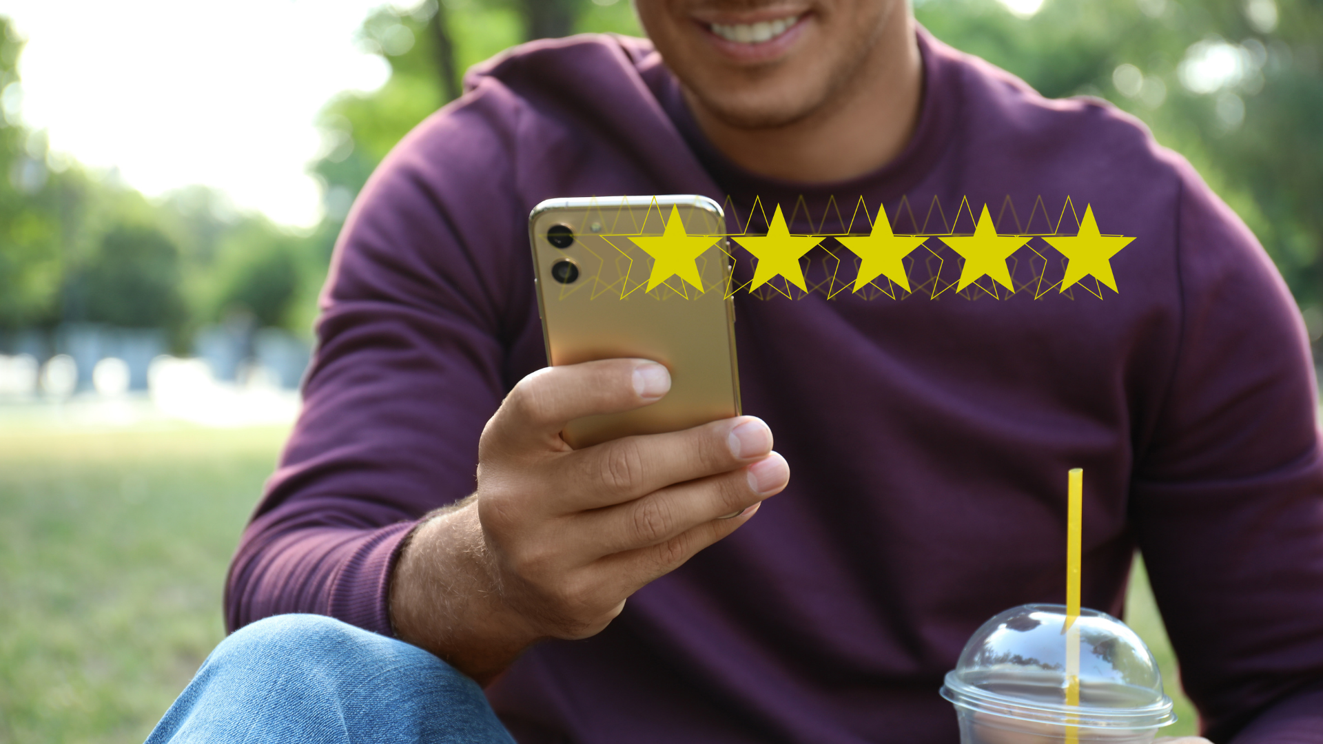 Un homme est assis dans l'herbe et regarde son téléphone portable.