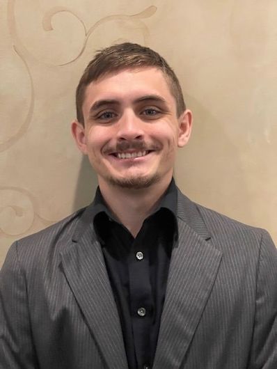 A young man with a beard and mustache is smiling for the camera.