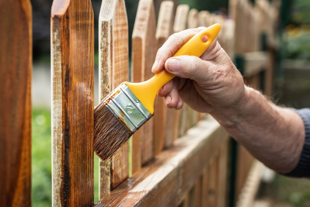 Hand painting a wooden fence with a yellow brush outdoors