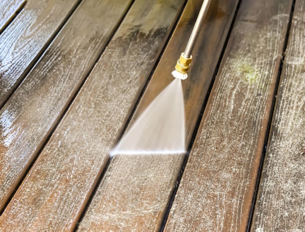 Close-up of a hose nozzle spraying water across wet wooden deck boards.