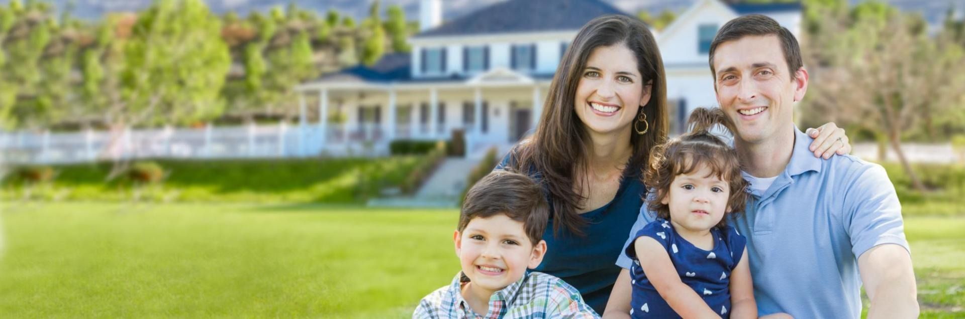Smiling family of four posing on a lawn in front of a large house