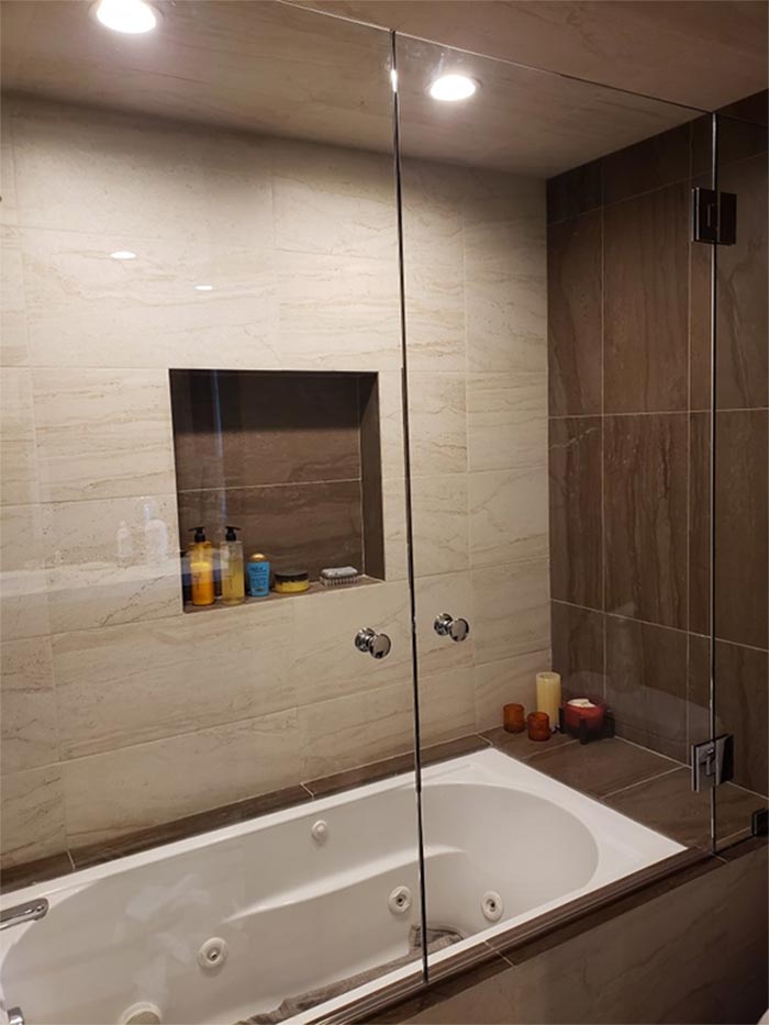 Bathroom with a white bathtub, glass shower door, and tiled walls.