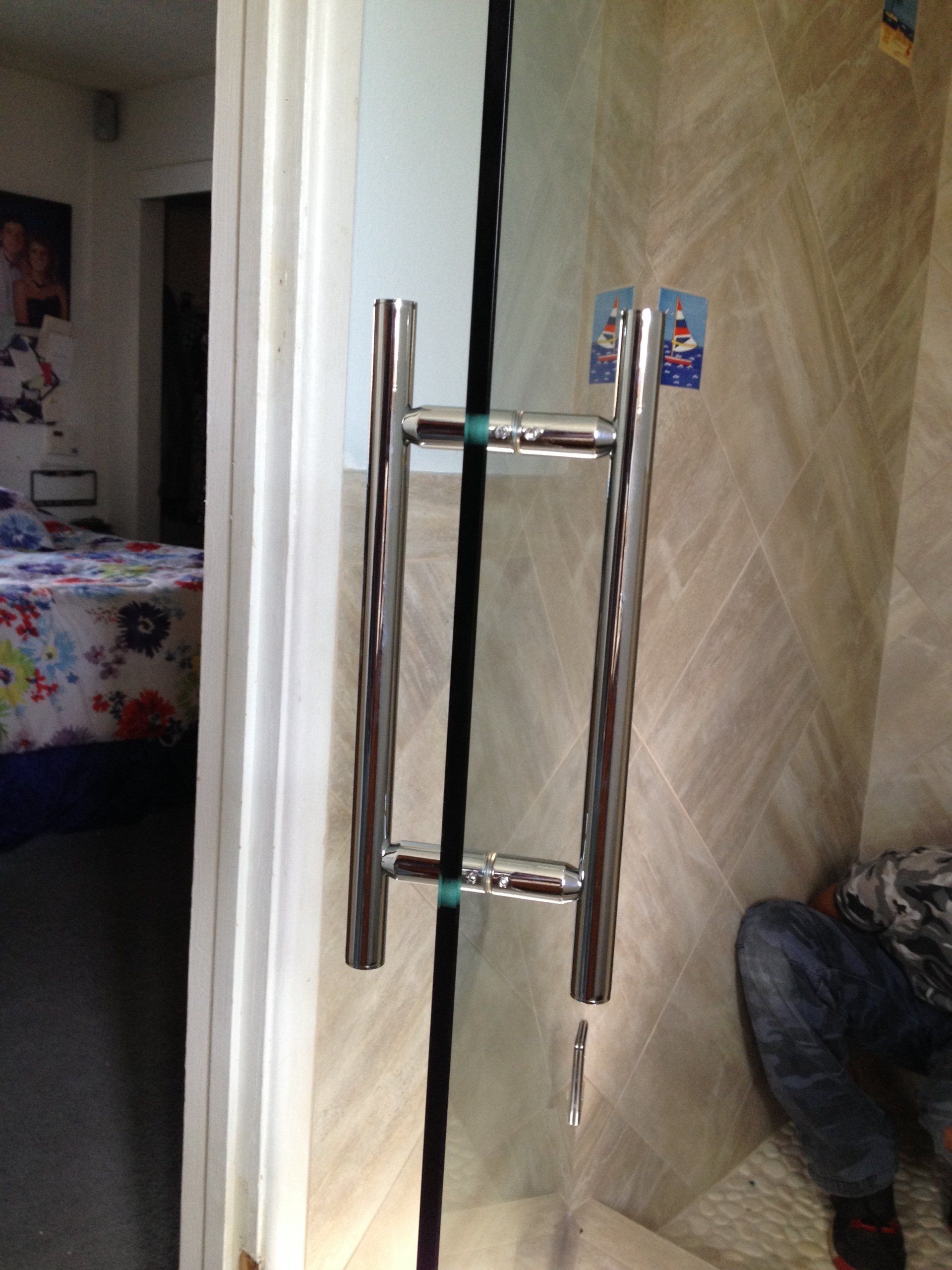 Glass shower door with a chrome handle and the bedroom in the background.