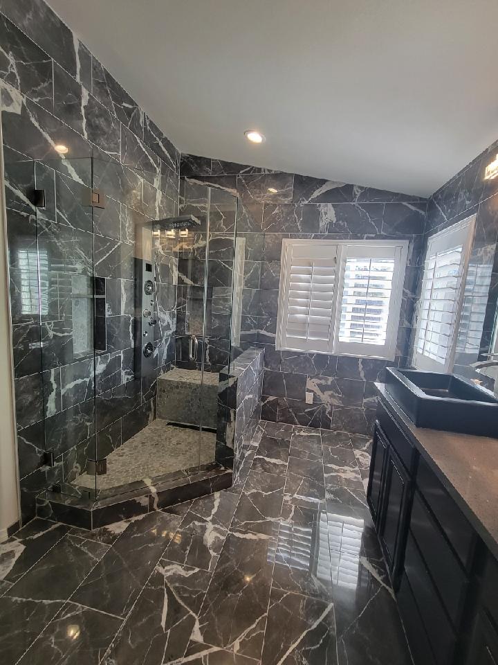 Modern bathroom with black marble tile, glass shower, and dark vanity.