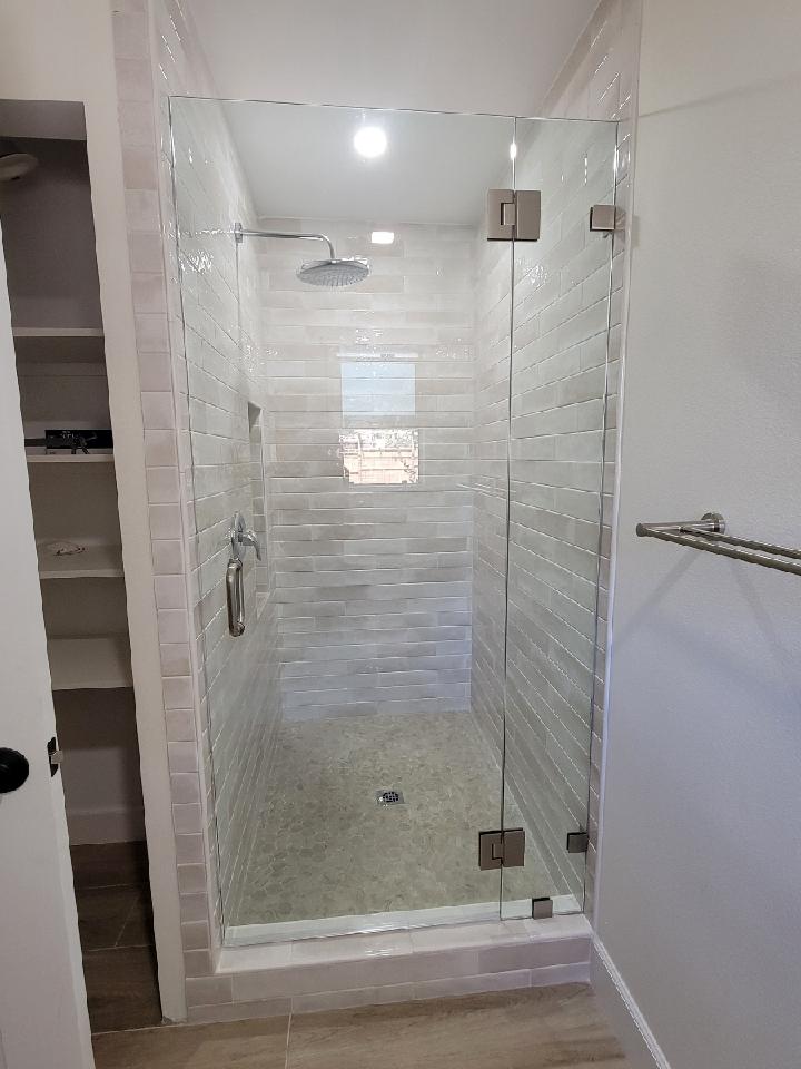 Glass shower with textured tile, silver fixtures, and a white border.