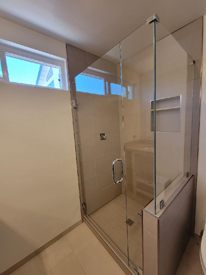 A modern shower with glass doors, tan tile walls, and a small window above.