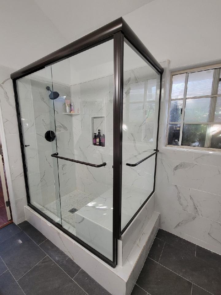 Modern shower with dark bronze trim and glass doors, white marble tile, and a grab bar.