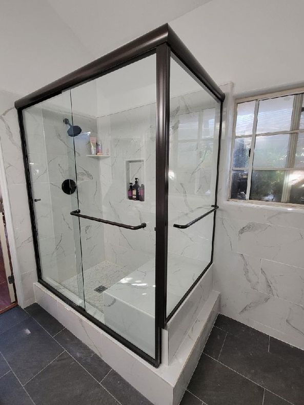 Modern corner shower with dark frame, glass doors, marble-look tile, and grab bars.