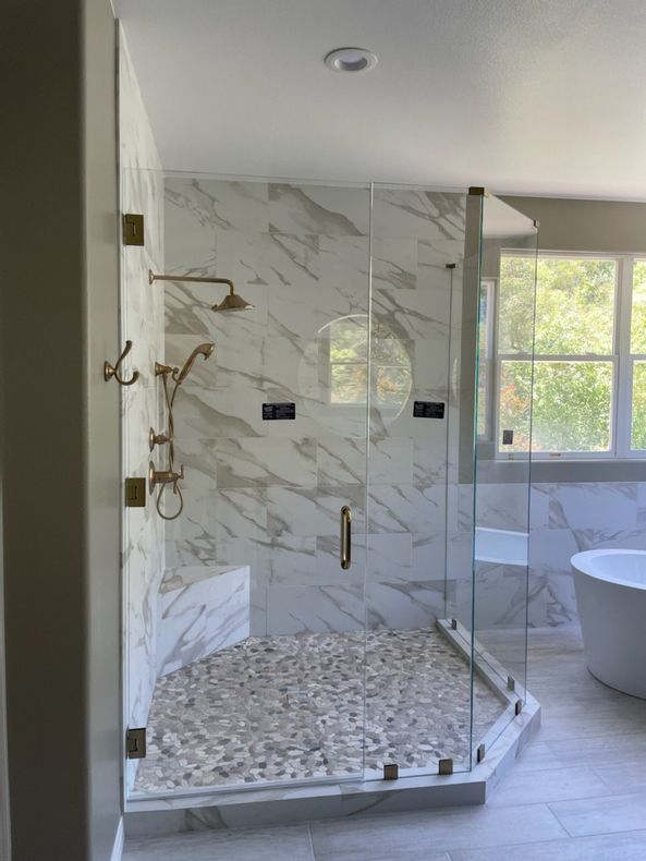 Luxurious marble shower with glass doors, pebble floor, and gold fixtures.