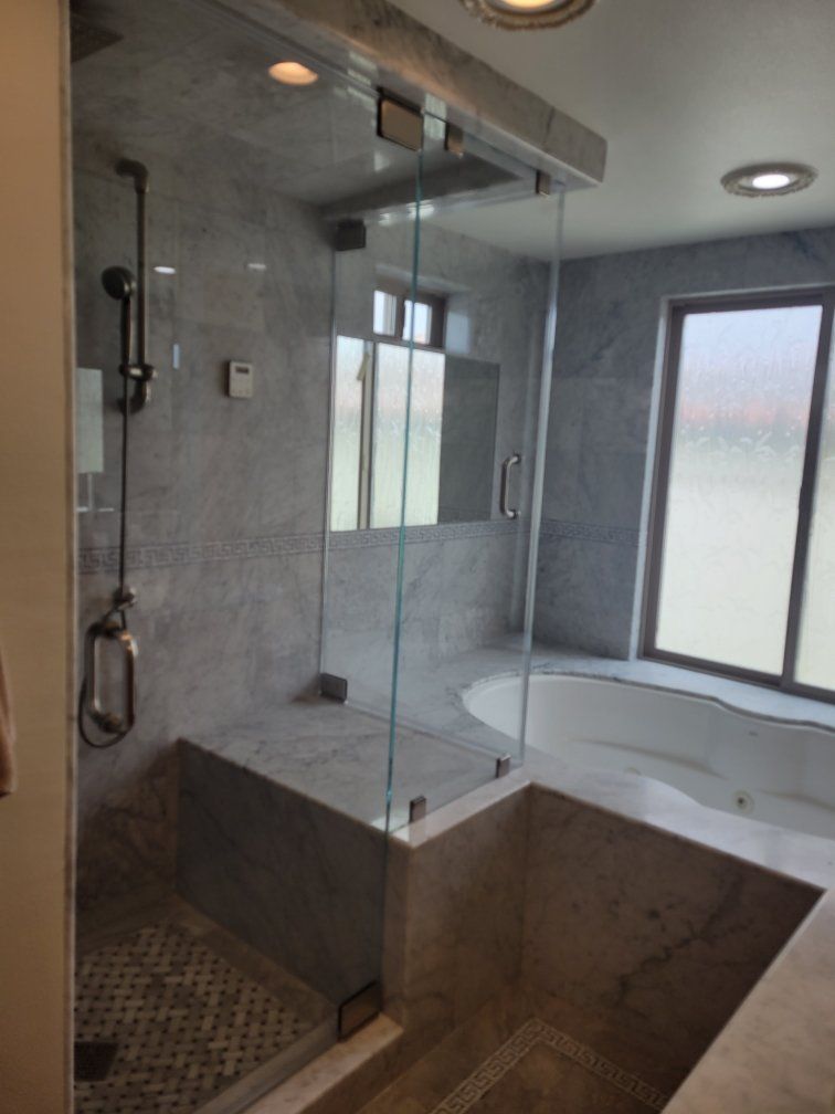 Modern bathroom with gray tiled walls, glass shower, and built-in tub near a window.