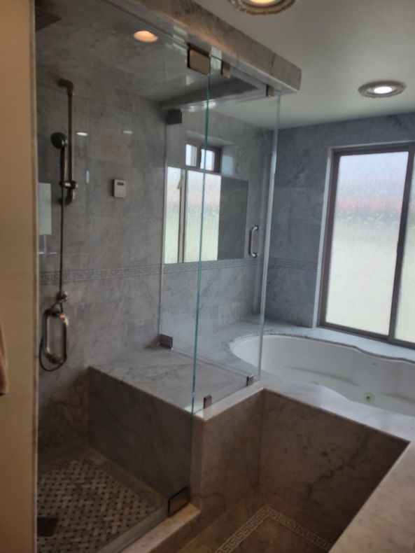 Modern bathroom with glass shower enclosure, gray marble tile, and built-in tub.
