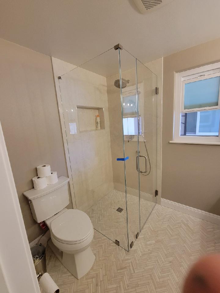 Bathroom with glass shower, toilet, window, and neutral-colored walls and floor.