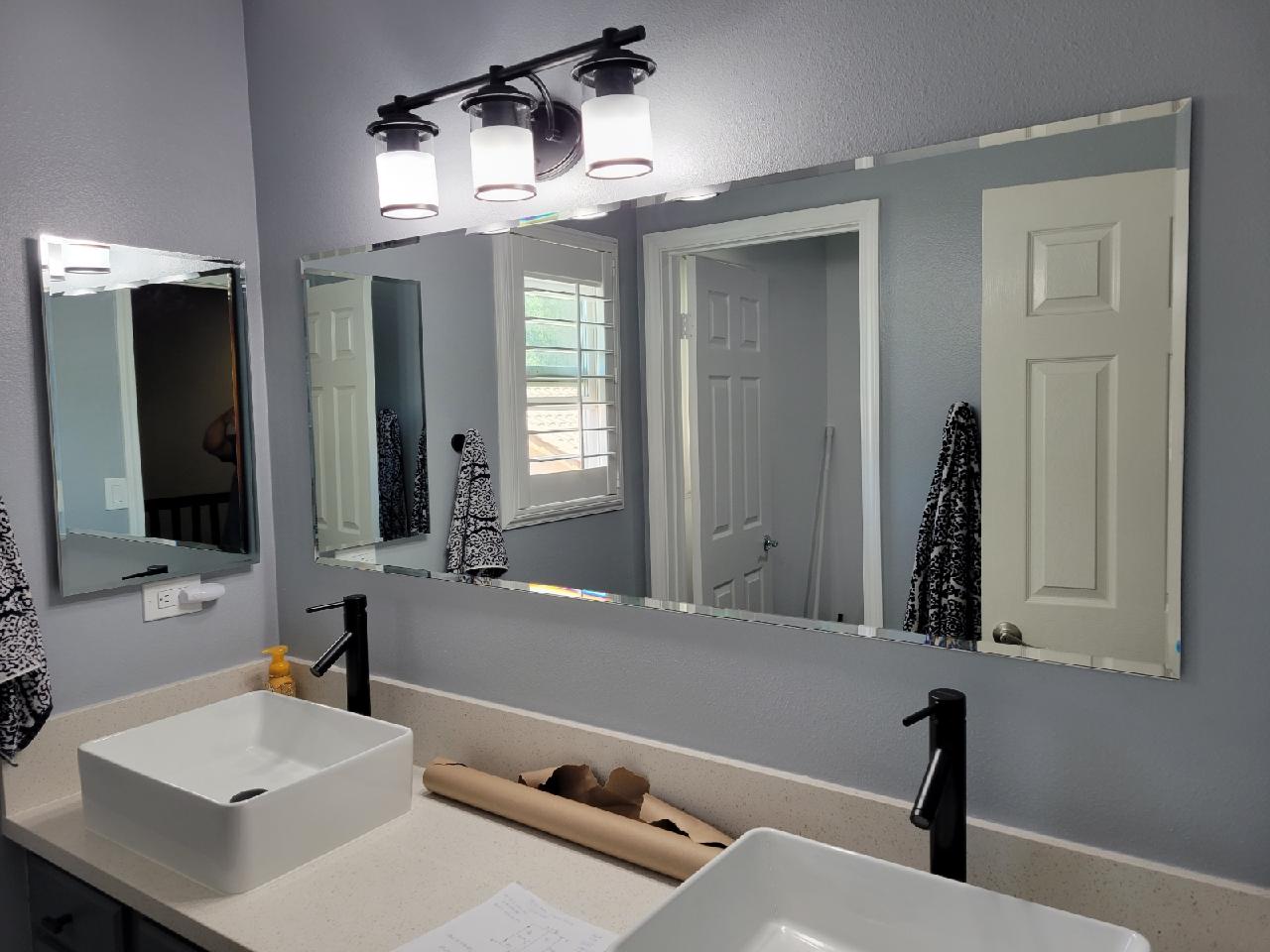 Bathroom with dual sinks, large mirror, and black fixtures. Grey walls.