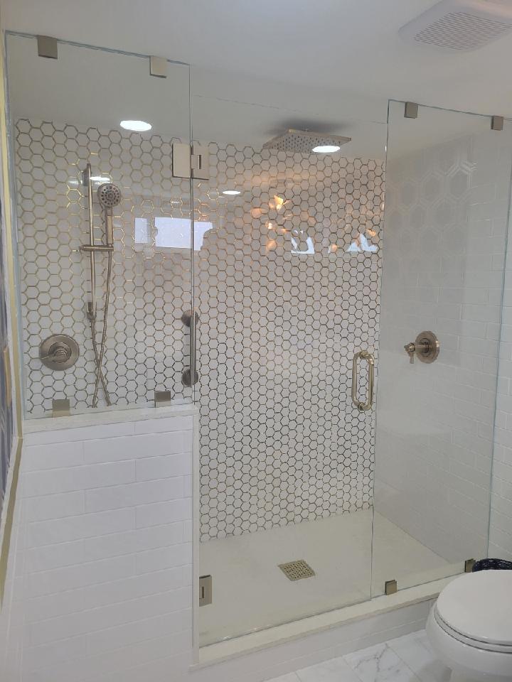 Glass-enclosed shower with white honeycomb tile walls, silver fixtures, and glass door.