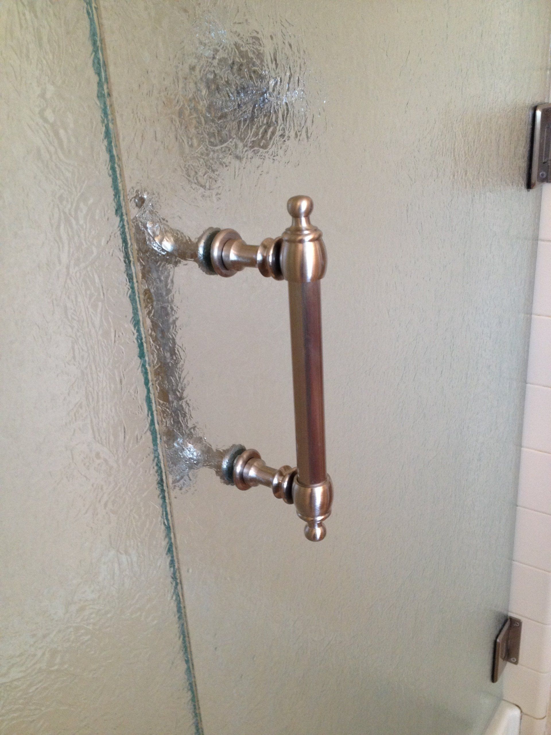 Antique bronze shower door handle on textured glass.