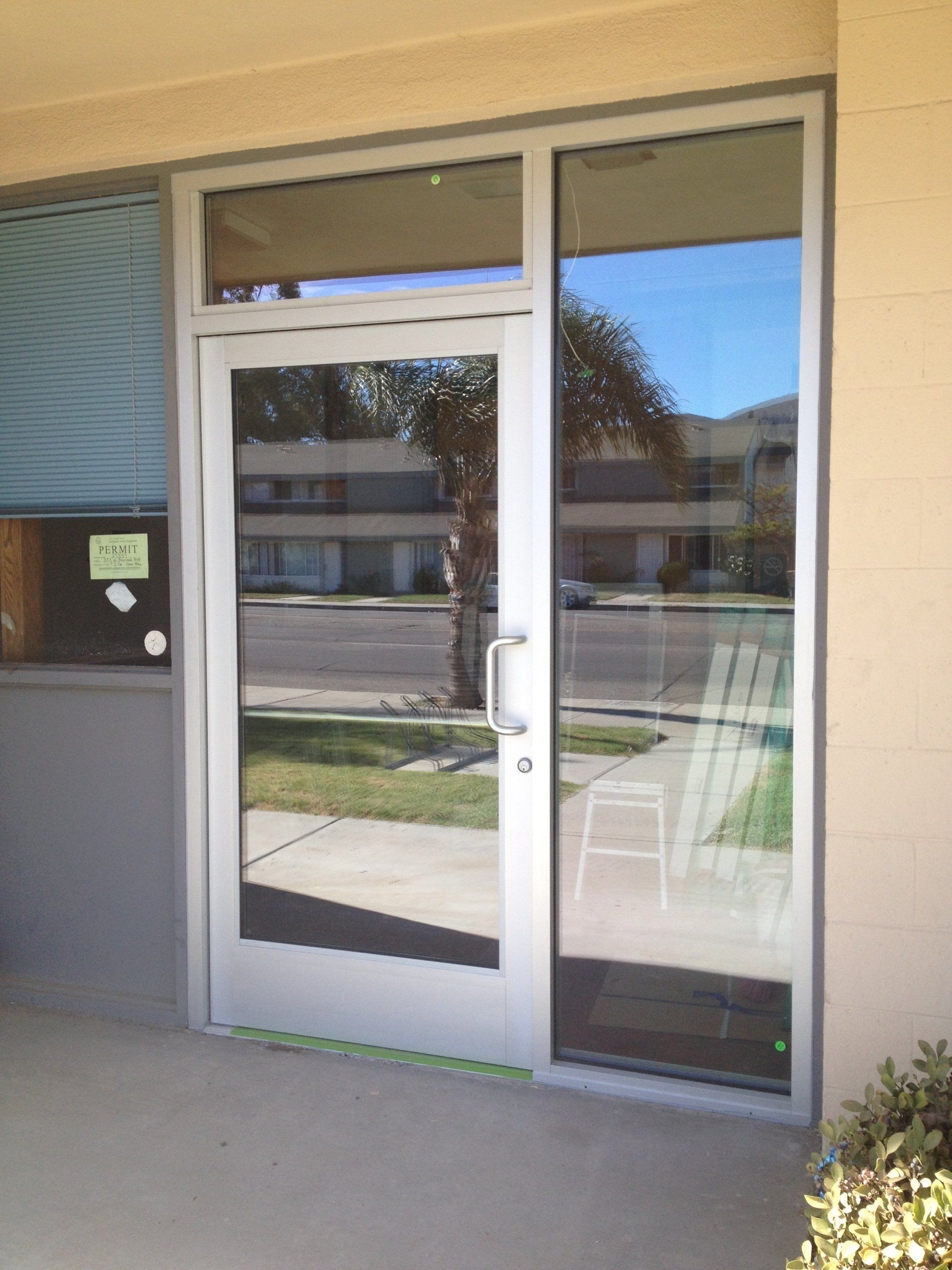 Glass door with sidelight, reflecting street scene. Light-colored building exterior.
