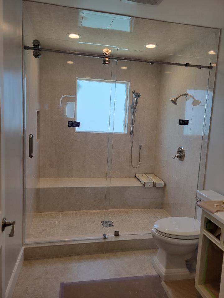 Bathroom with glass shower enclosure, bench, and toilet. Beige tile, white walls, and a small window.
