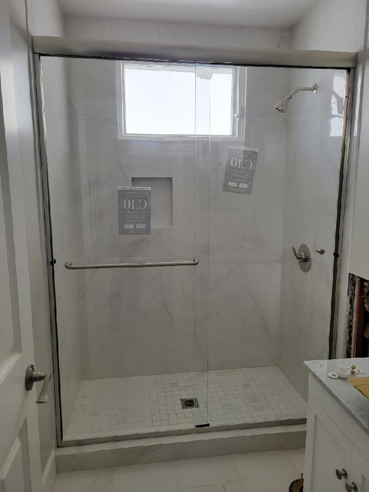 Shower with glass doors, white tile, and chrome fixtures. A window is visible inside.