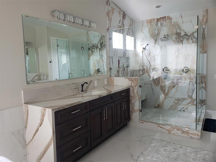 Bathroom with marble walls and countertop, dark wood vanity, glass shower enclosure.