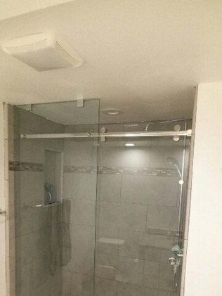 Shower with glass doors and gray tiled walls. A fan is visible in the ceiling.