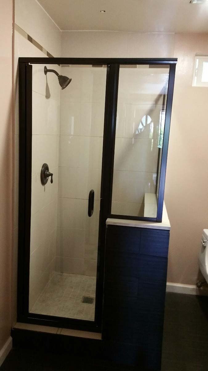 Black framed shower with glass doors, set atop a dark blue cabinet, in a bathroom.