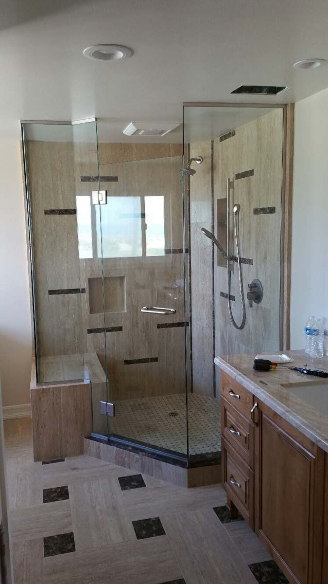 A modern bathroom with a glass shower, light-colored tile, and wooden vanity.