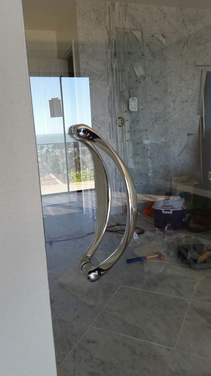 Glass shower door with curved chrome handle, overlooking a city view.