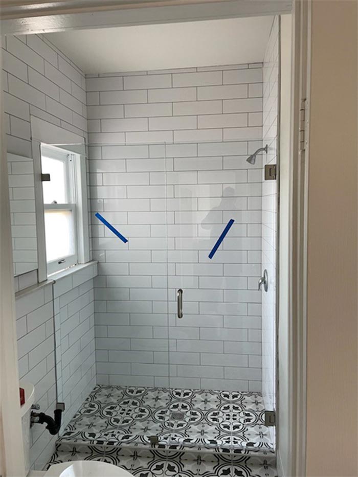 Bathroom with glass shower door, white subway tiles, patterned floor tiles, and a window.