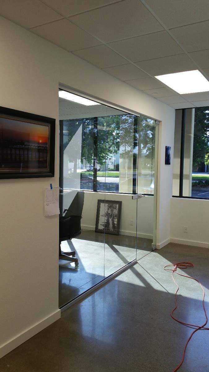 Office interior with glass walls, sunlight, artwork, and an open doorway.
