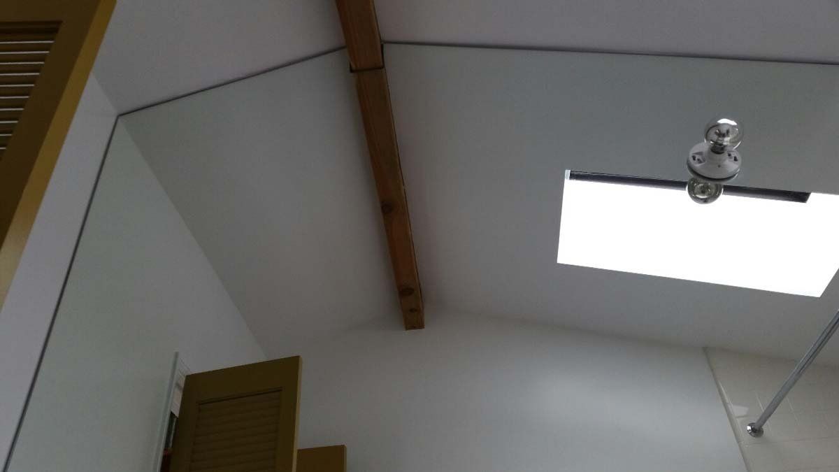 Bathroom ceiling with a skylight, wooden beam, and a light fixture.