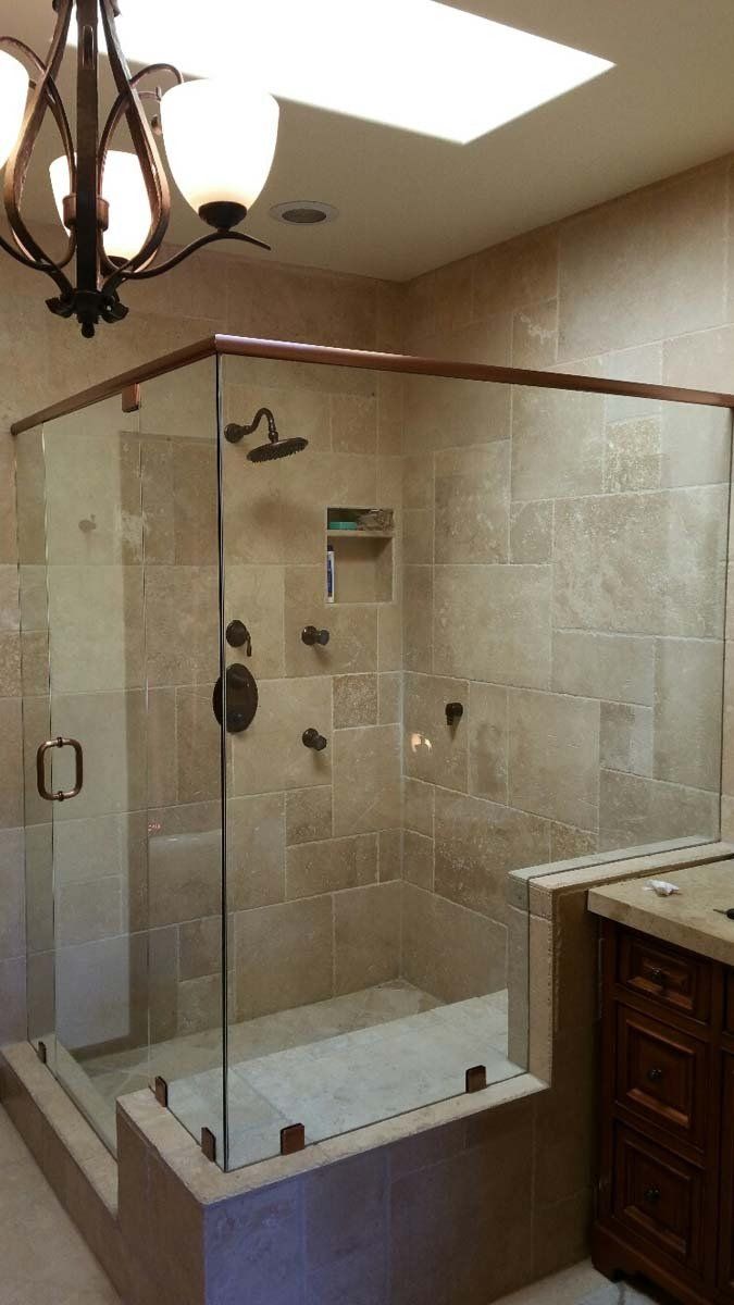 Bathroom shower with glass enclosure, tan tiles, copper fixtures, and a skylight.