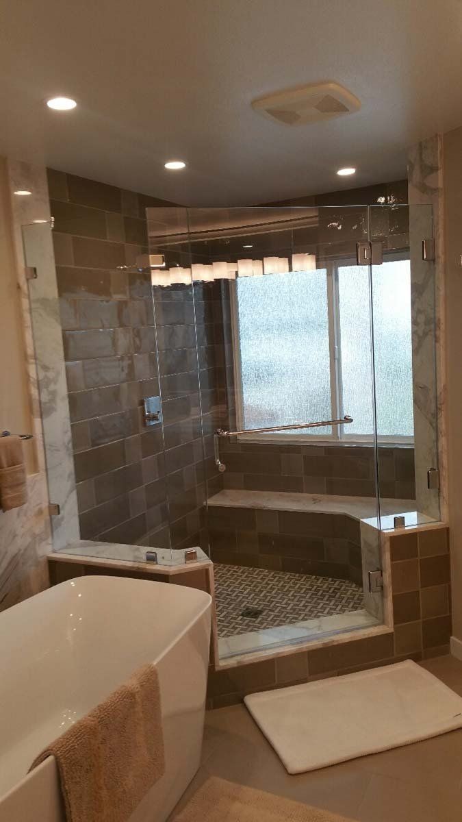 Bathroom with a glass-enclosed shower, built-in seat, and large window. Tub in foreground.