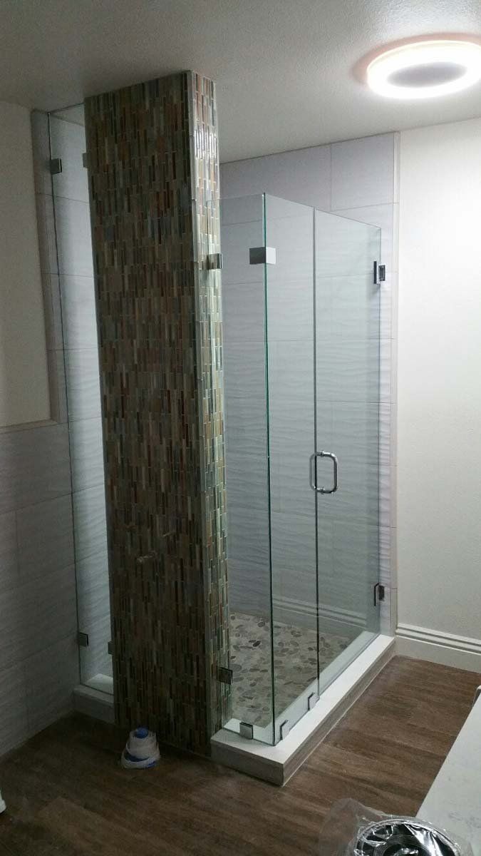 Modern bathroom with glass shower doors and stone accent wall. White tile and wood-look flooring.