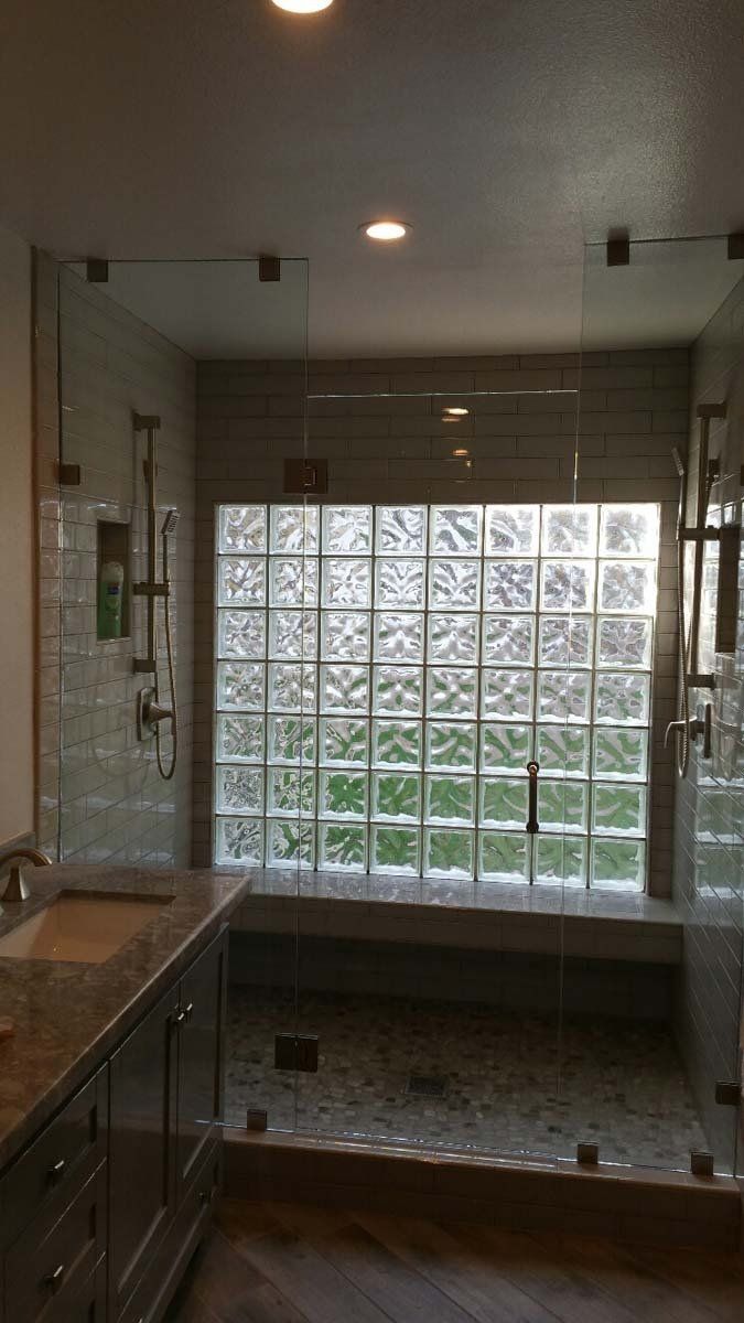 Modern bathroom with glass shower, glass block window, and stone floor.