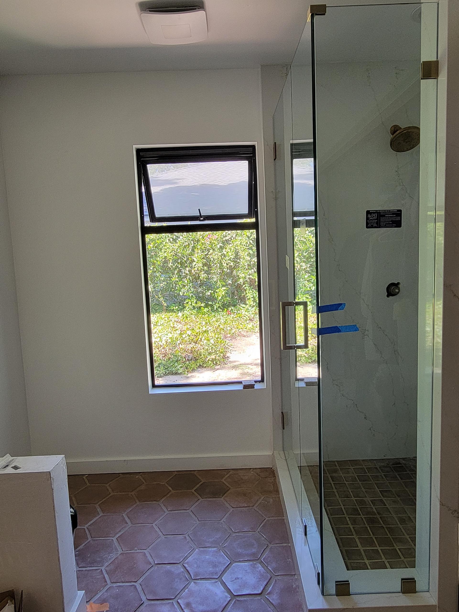 Bathroom with hexagonal terracotta floor tiles, glass shower, and a window overlooking greenery.