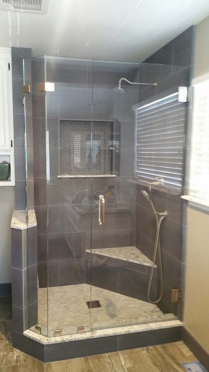 Glass-enclosed shower with gray tile walls, a built-in corner seat, and a silver shower head.