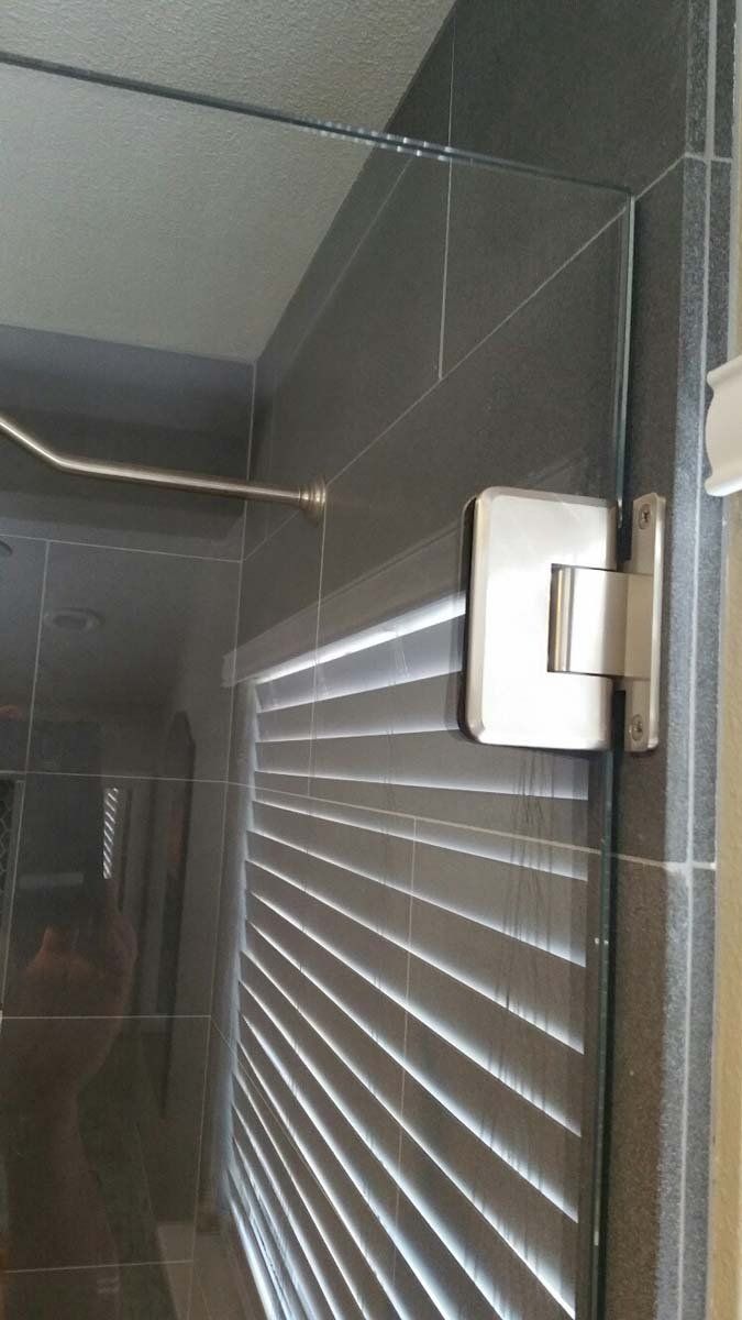 Silver hinge on a black glass shower door. Black tile wall.