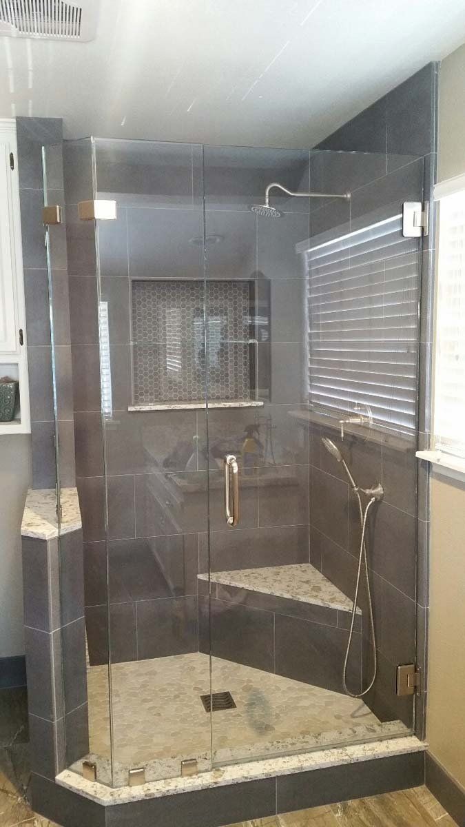 Glass-enclosed shower with dark tile and stone accents. Window with blinds is visible.