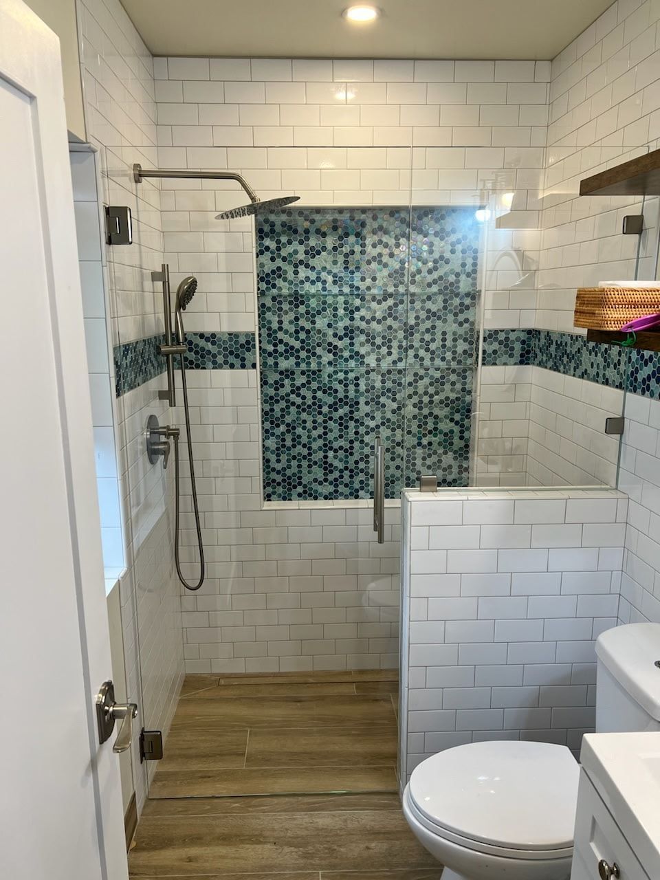 Small, modern bathroom with glass shower, white subway tile, and wood-look tile floor.