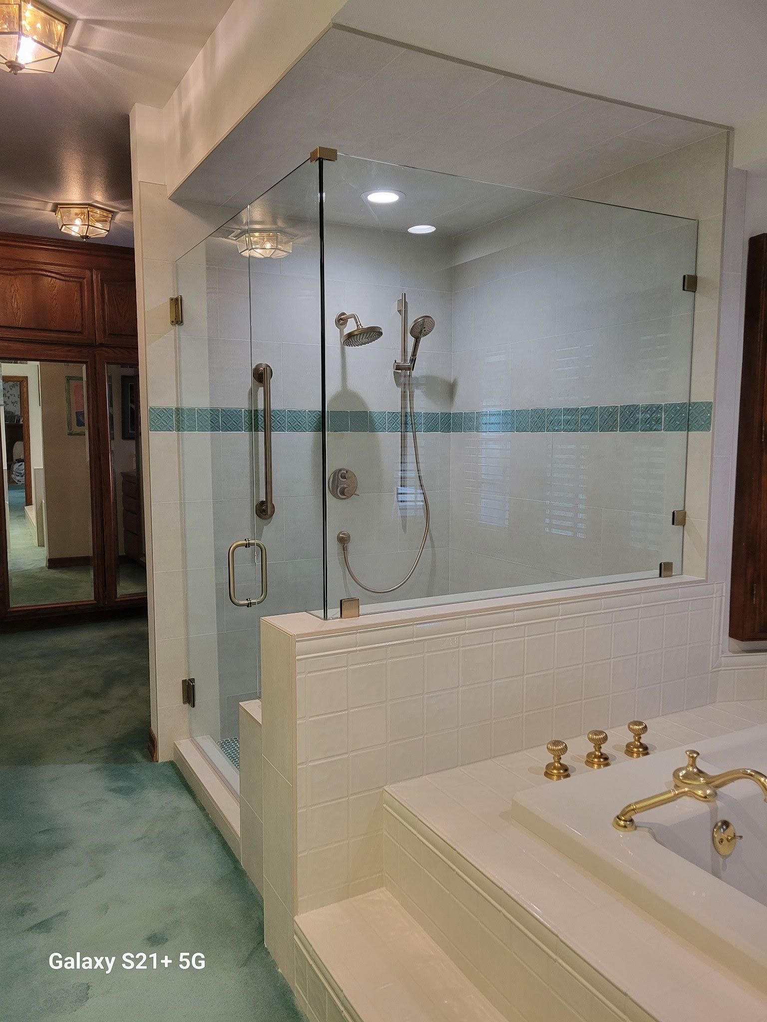 A modern bathroom with a glass shower and a white bathtub. Teal accents and gold fixtures.