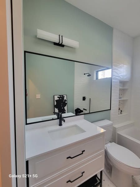 Bathroom with white vanity, black framed mirror, green accent wall, and white toilet.