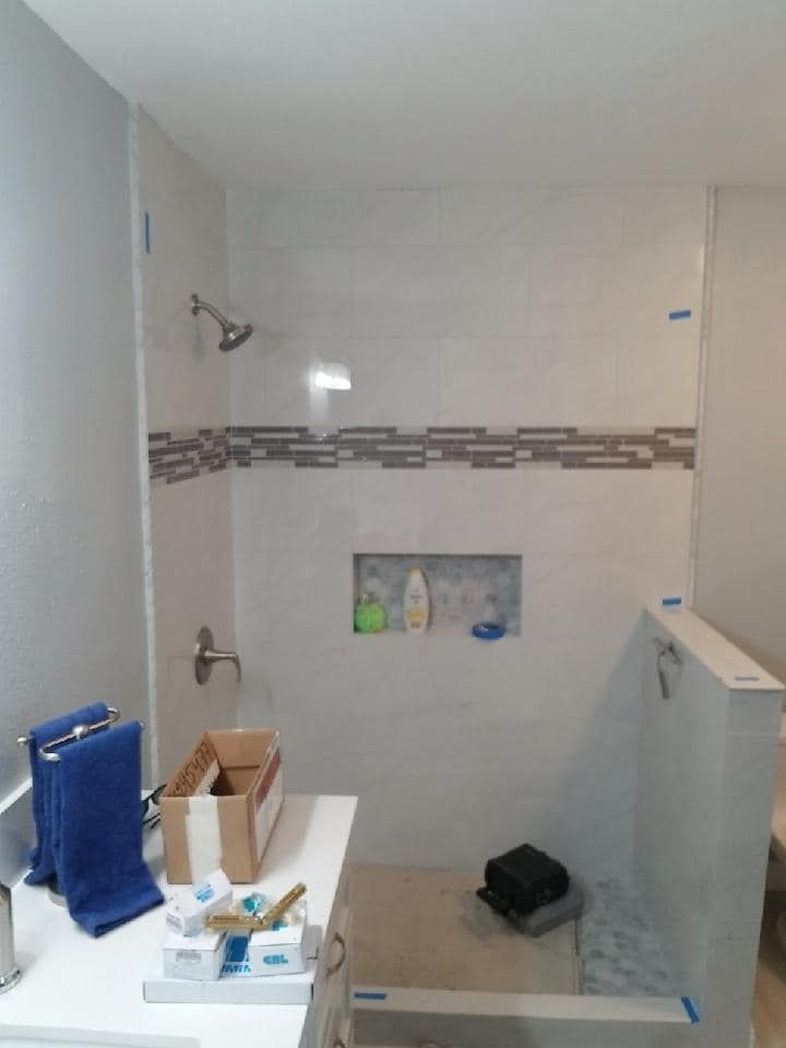 Bathroom with gray and white tile shower, built-in shelf, and blue towels on the vanity.
