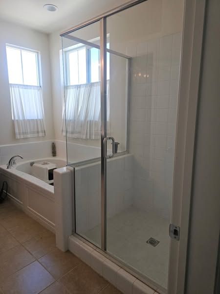 Bathroom with a glass shower, white tub, and windows with curtains.