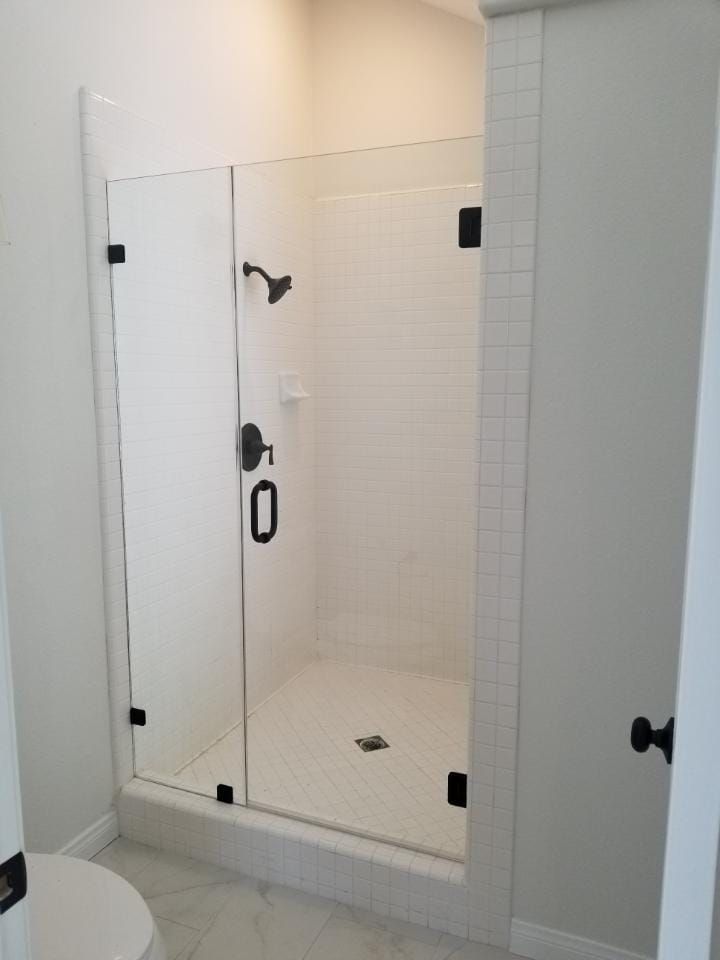 White tiled shower with glass door and black hardware.